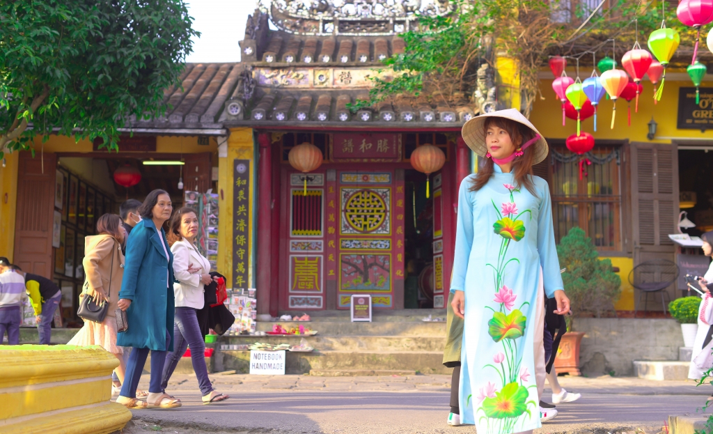 A tourist in Aodai and traditional hats in the old town of Hoi An, Vietnam