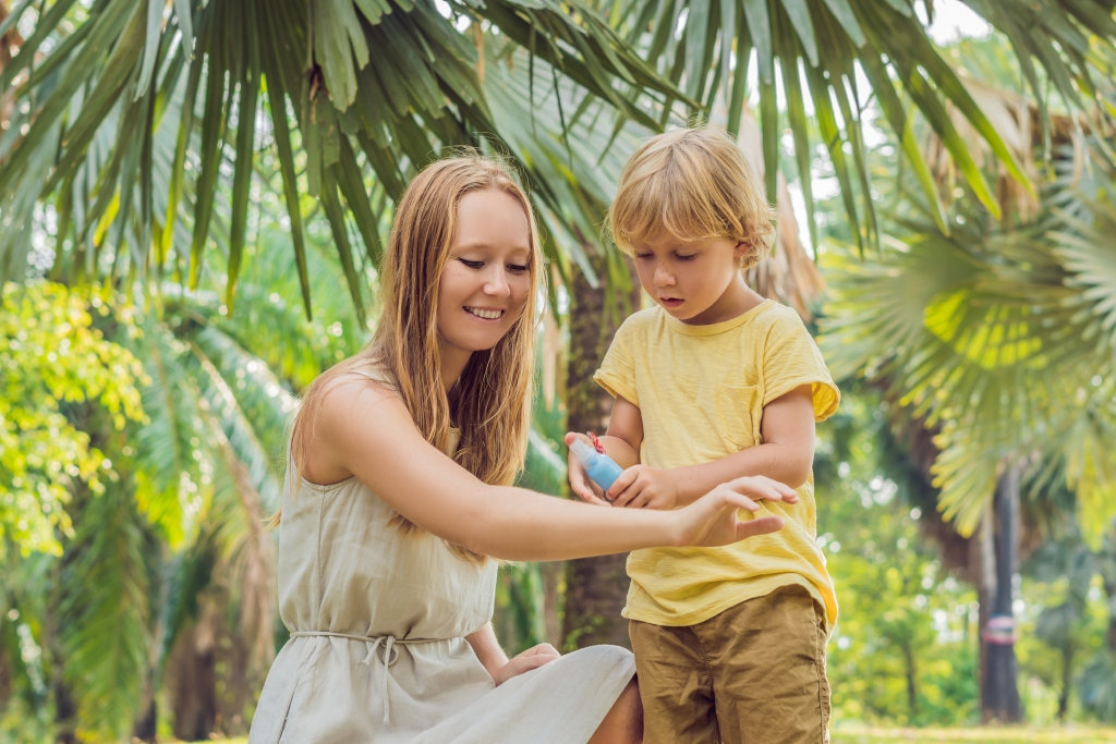 Mom and son spraying insect repellent on skin outdoor.